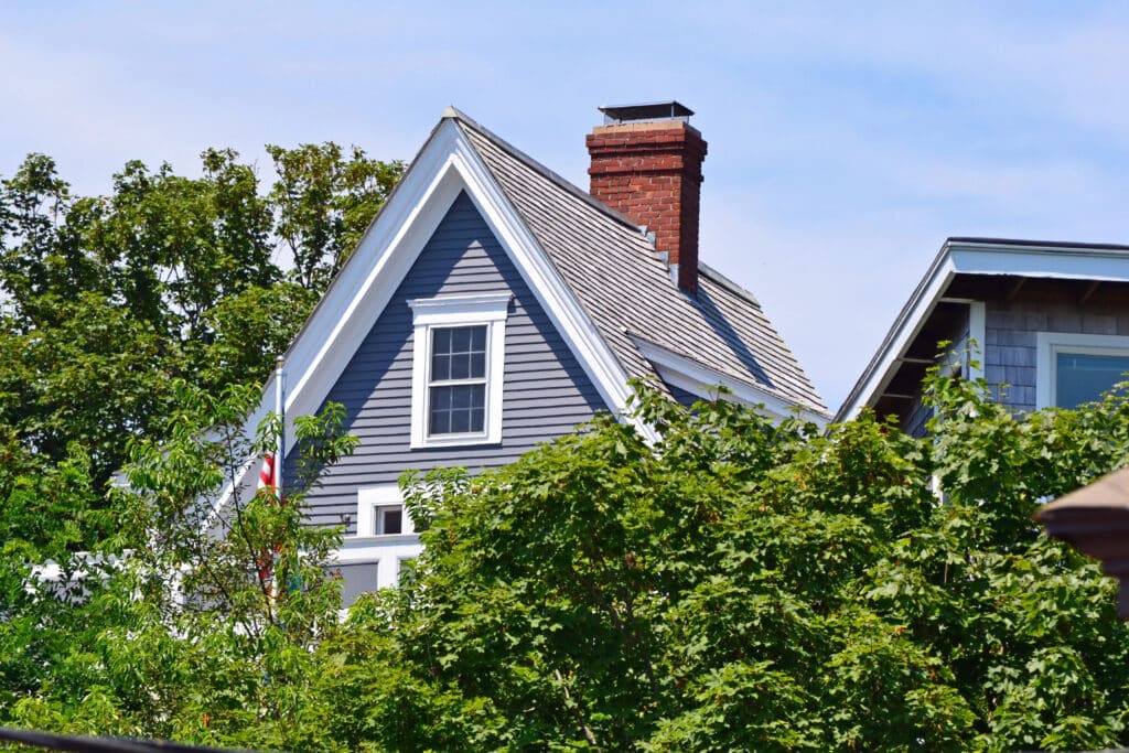 Depositphotos_31639947_XL Gabled roof of a gray house with a brick chimney, surrounded by lush green trees on a clear day. | Sky Rye Design Gabled roof of a gray house with a brick chimney, surrounded by lush green trees on a clear day.
