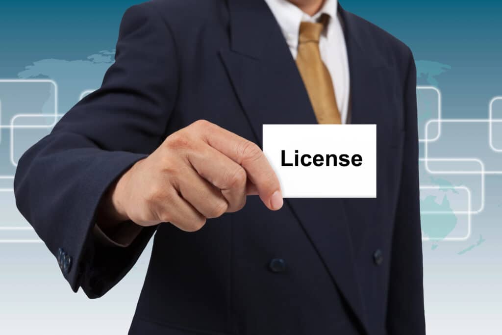 Businessman in suit presenting a card labeled License against a digital background.