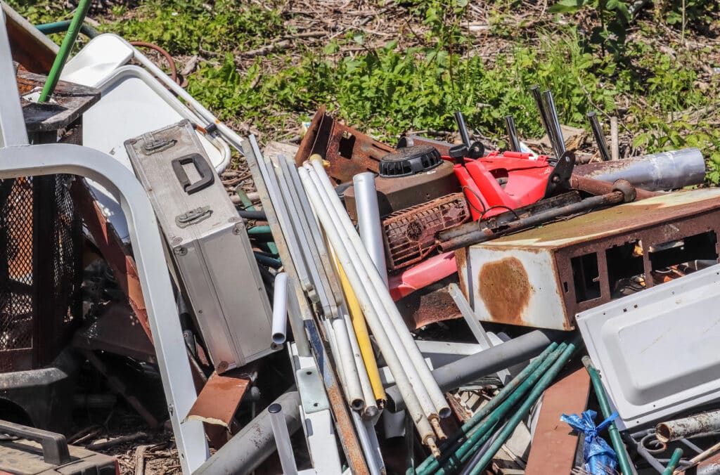 Depositphotos_379162744_XL Pile of mixed scrap metal and tools on grass, including pipes and a rusty appliance in sunlight. | Sky Rye Design Pile of mixed scrap metal and tools on grass, including pipes and a rusty appliance in sunlight.