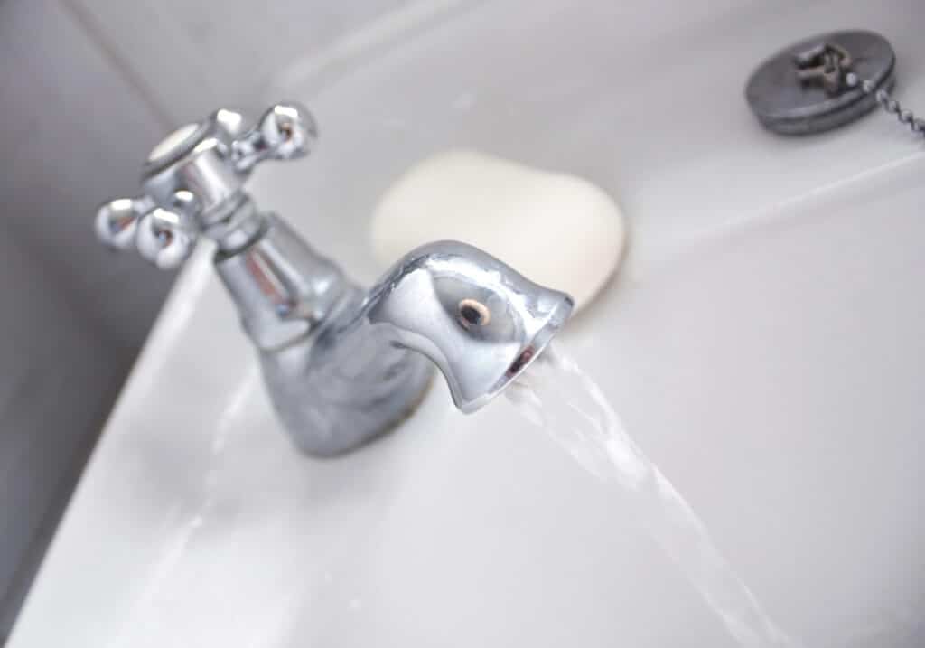 Depositphotos_5926664_XL Close-up of water flowing from a chrome bathroom faucet into a white sink, with a bar of soap in the background. | Sky Rye Design Close-up of water flowing from a chrome bathroom faucet into a white sink, with a bar of soap in the background.