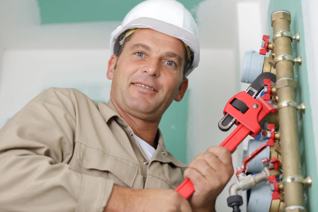 Depositphotos_712724266_XL Plumber working with a wrench on pipes, wearing a hard hat, in a building under construction or renovation. | Sky Rye Design Plumber working with a wrench on pipes, wearing a hard hat, in a building under construction or renovation.