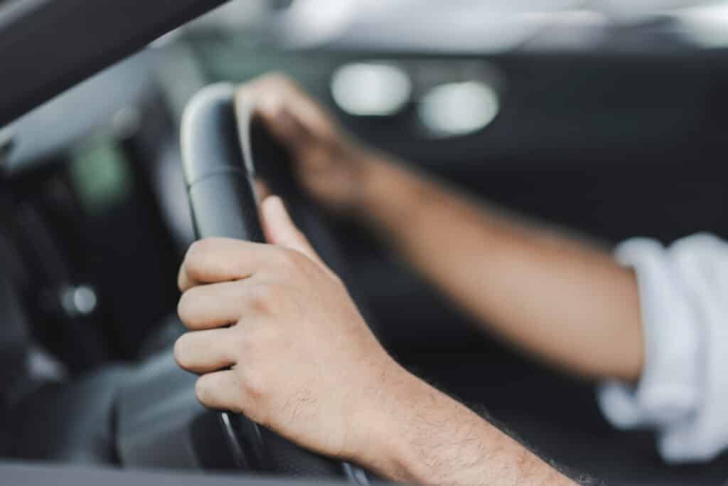 Close-up of hands gripping a car steering wheel, indicating a focus on driving and automotive control.