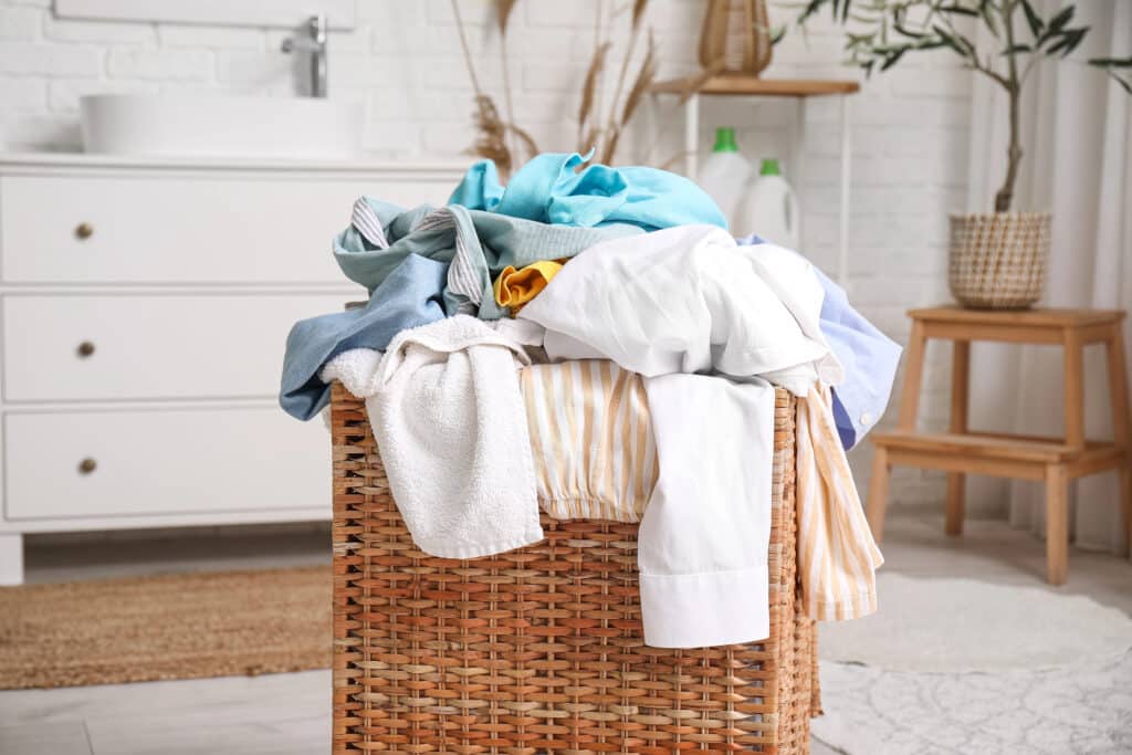 Depositphotos_758587158_XL Laundry basket with overflowing clothes in a bright, cozy room. | Sky Rye Design Laundry basket with overflowing clothes in a bright, cozy room.
