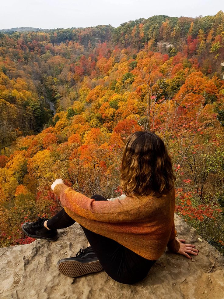 Dundas Peak_ The best place to see fall colors in Canada _ Ilse on the go Person sitting on cliff edge, overlooking vibrant autumn forest with colorful foliage in shades of red, orange, and yellow. | Sky Rye Design Person sitting on cliff edge, overlooking vibrant autumn forest with colorful foliage in shades of red, orange, and yellow.