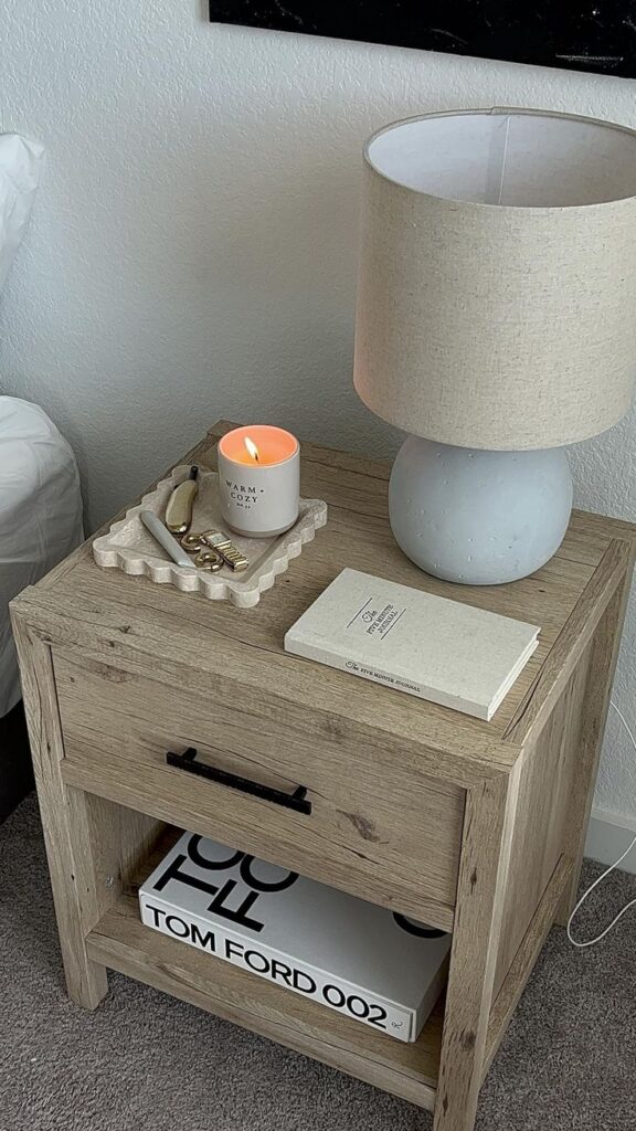 Elevate your bedroom with these essentials Wooden nightstand with a lamp, candle, and books, creating a cozy bedroom ambiance. | Sky Rye Design Wooden nightstand with a lamp, candle, and books, creating a cozy bedroom ambiance.
