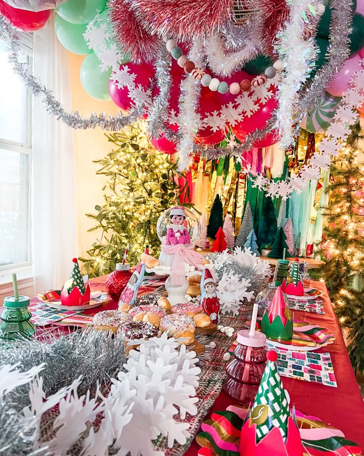 Festive Christmas party table with treats, decorations, and elf-themed items under colorful decorations and tinsel.