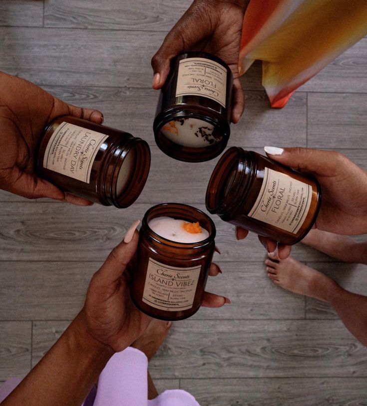 FULLY STOCKED Luxury Aromatherapy Nationwide Shipping 📸 luis_fidel Four hands hold brown jars of scented candles labeled Island Vibez, Floral, and Laundry Day on a wooden floor. | Sky Rye Design Four hands hold brown jars of scented candles labeled Island Vibez, Floral, and Laundry Day on a wooden floor.