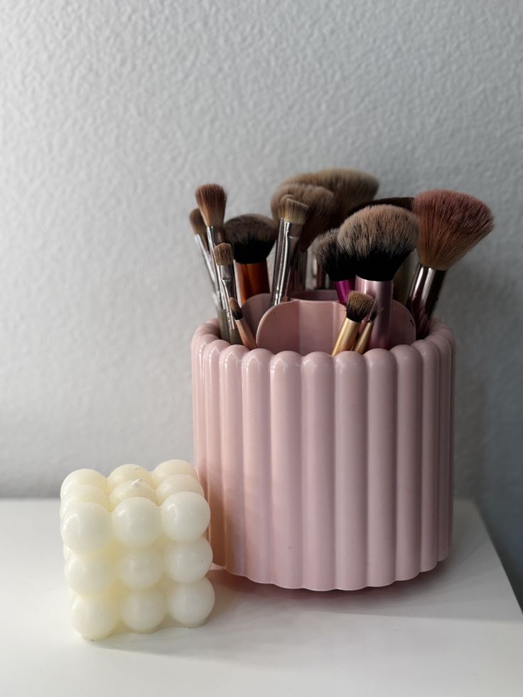 Favorite makeup brush holder Pink makeup brush holder with various brushes next to a white bubble candle on a white surface. | Sky Rye Design Pink makeup brush holder with various brushes next to a white bubble candle on a white surface.