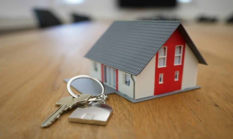 Model house and keys on a wooden table symbolizing real estate and home ownership concepts.