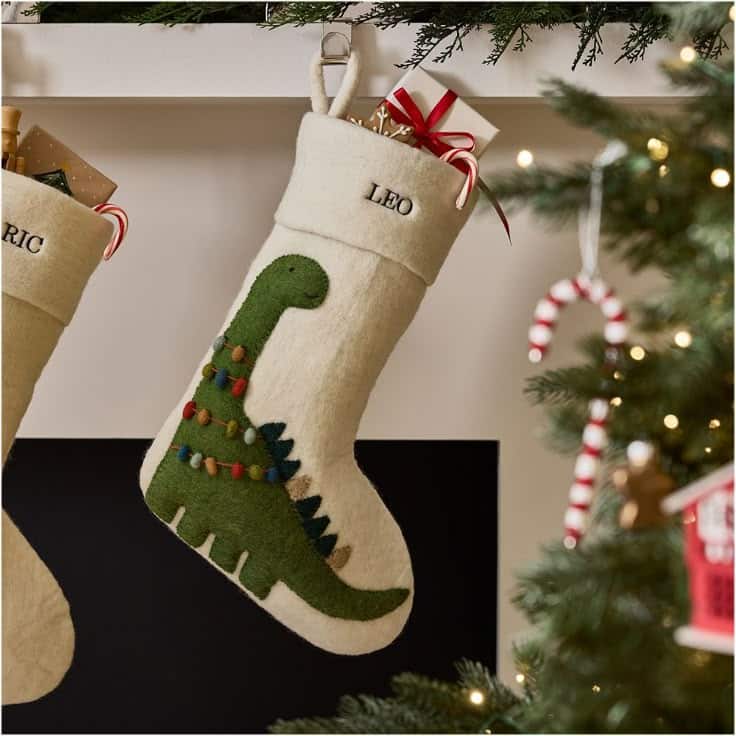 Felt Dinosaur Stocking Personalized Christmas stocking with dinosaur design hanging by a decorated tree, filled with gifts and candy canes. | Sky Rye Design Personalized Christmas stocking with dinosaur design hanging by a decorated tree, filled with gifts and candy canes.