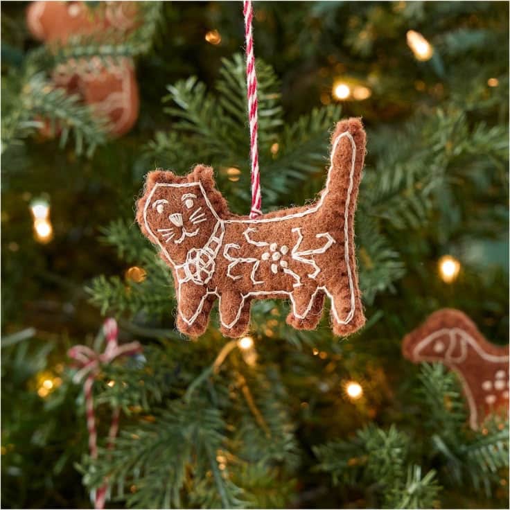 Felt Gingerbread Collection Felt cat Christmas ornament with white stitching hangs on a festive tree with lights. | Sky Rye Design Felt cat Christmas ornament with white stitching hangs on a festive tree with lights.