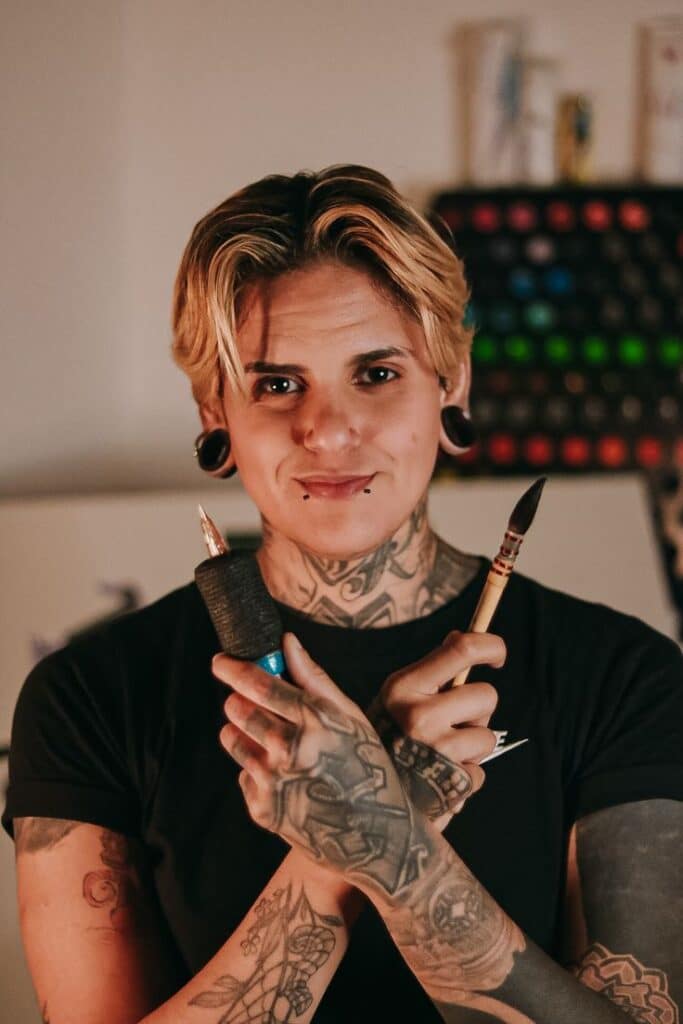 Tattoo artist with tattoo machine and brush in hand, showing body art and expression.