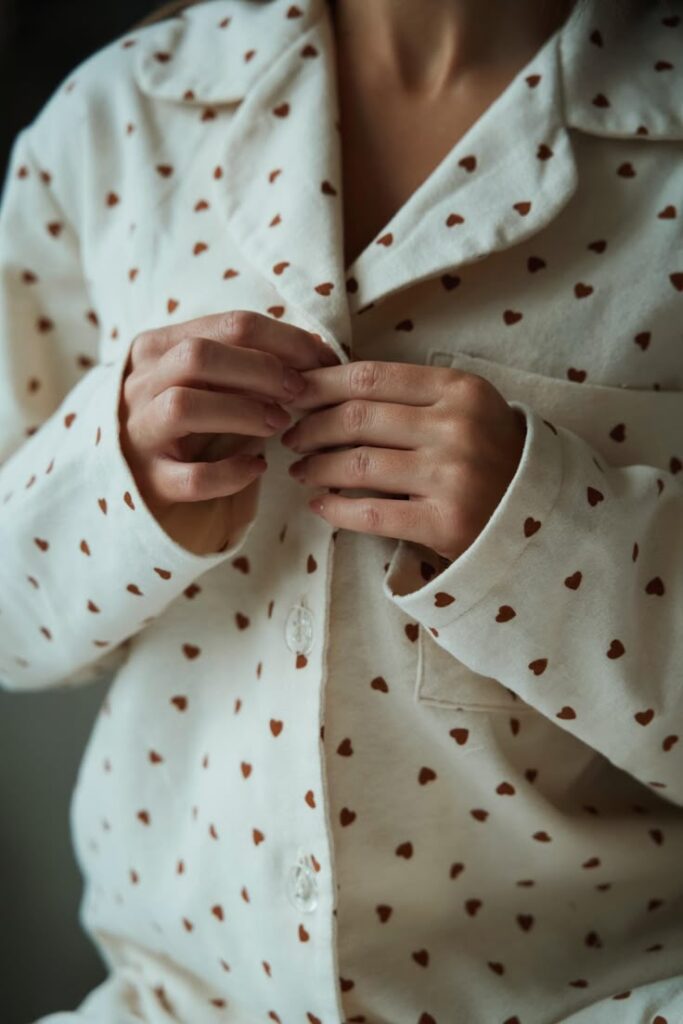 Person buttoning heart-patterned pajamas, showcasing cozy and stylish sleepwear design.