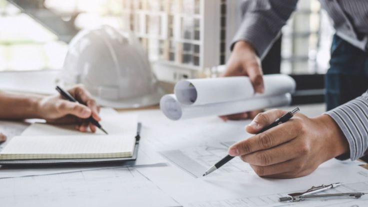 Architects reviewing blueprints and taking notes, planning a construction project with a focus on detailed design work.