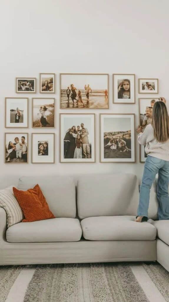 Gallery Wall Ideas_ Transform Your Blank Walls into a Stunning Masterpiece Woman arranging family photo gallery wall above beige sofa with decorative pillows in living room. | Sky Rye Design Woman arranging family photo gallery wall above beige sofa with decorative pillows in living room.