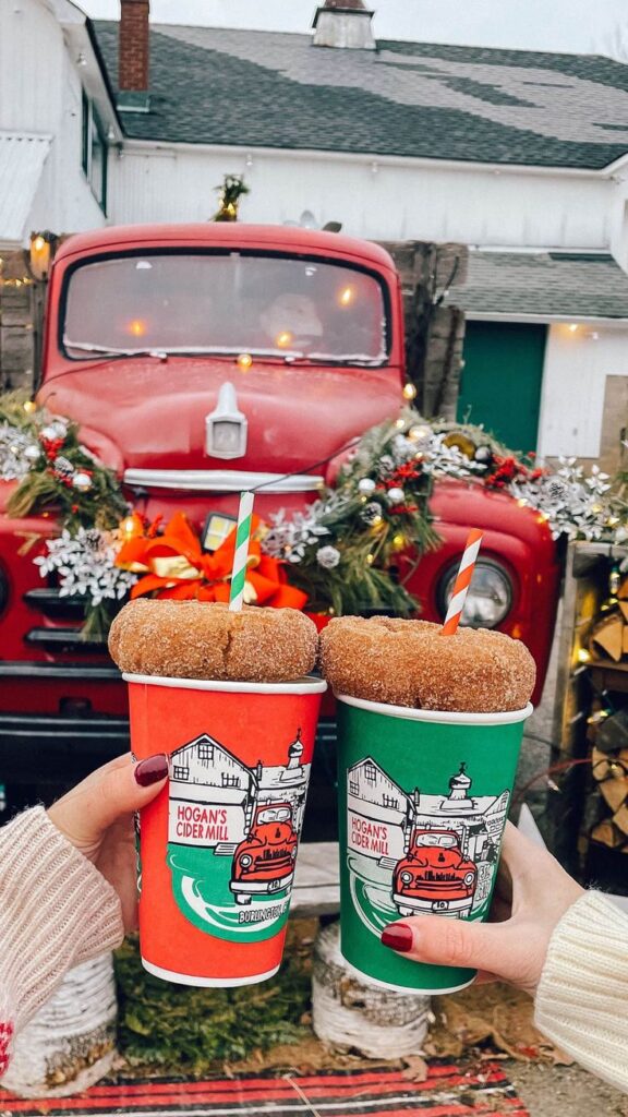 Gilmore Girls Connecticut Road Trip_ Holiday Getaway Two festive hot cider cups with donut tops in front of a decorated red vintage truck during winter holidays. | Sky Rye Design Two festive hot cider cups with donut tops in front of a decorated red vintage truck during winter holidays.