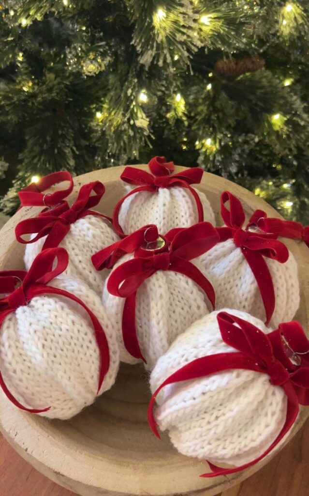 Hand Knit Cozy Ornaments Handmade Christmas ornaments with white knit texture and red bows in a wooden bowl by a festive tree. | Sky Rye Design Handmade Christmas ornaments with white knit texture and red bows in a wooden bowl by a festive tree.