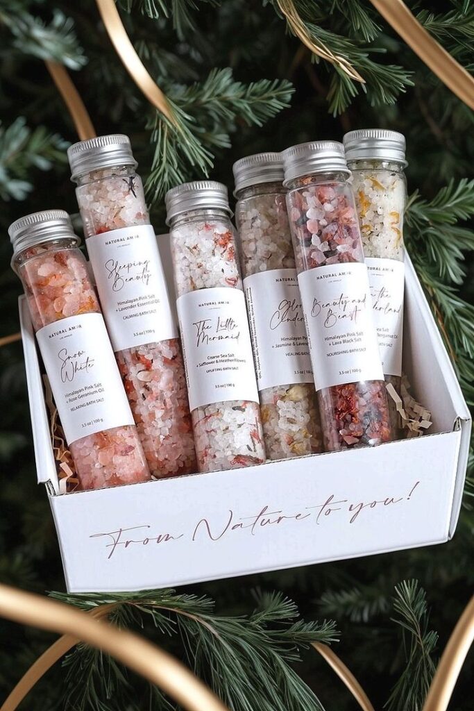 Gift box of six bath salt vials with natural ingredients, displayed on a green leafy background.