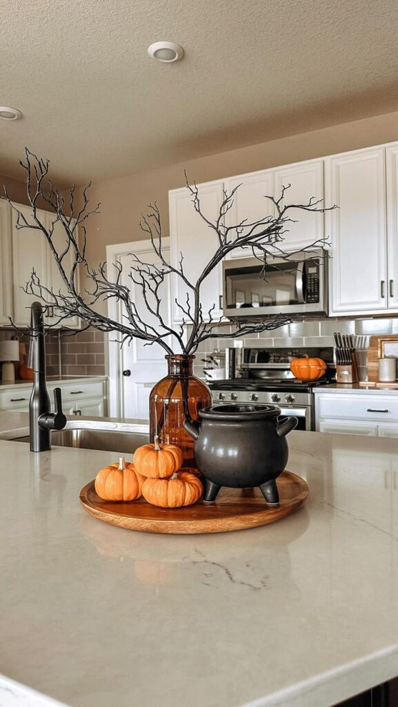 Modern kitchen with Halloween decor: small pumpkins, black cauldron, and bare branches on a white countertop.