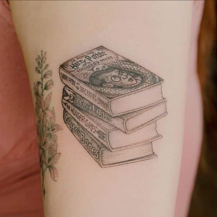 Harry Potter Jogos Vorazes Percy Jackson e Senhor dos Anéis tattoo Tattoo of stacked books including Harry Potter on arm with floral design. | Sky Rye Design Tattoo of stacked books including Harry Potter on arm with floral design.