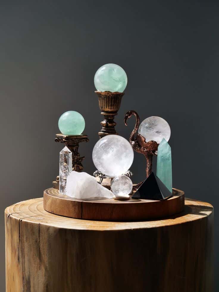 Decorative display of assorted crystals and glass orbs on a wooden stand under soft lighting.