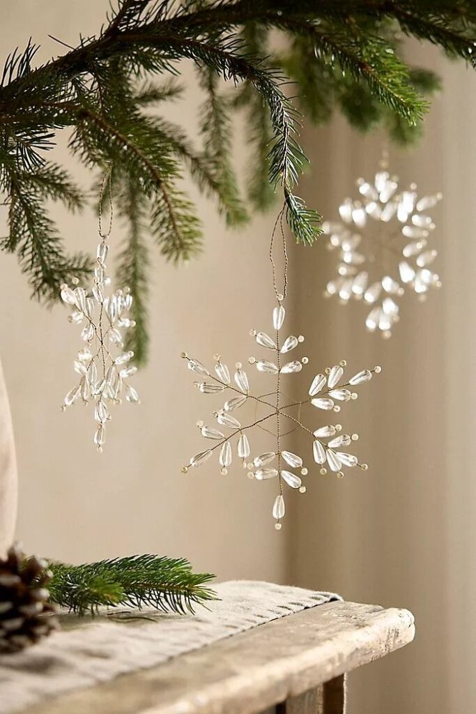 Holiday + Christmas Home Deฬcor Elegant glass snowflake ornaments hanging on a fir branch, enhancing festive holiday decor with a touch of sparkle. | Sky Rye Design Elegant glass snowflake ornaments hanging on a fir branch, enhancing festive holiday decor with a touch of sparkle.