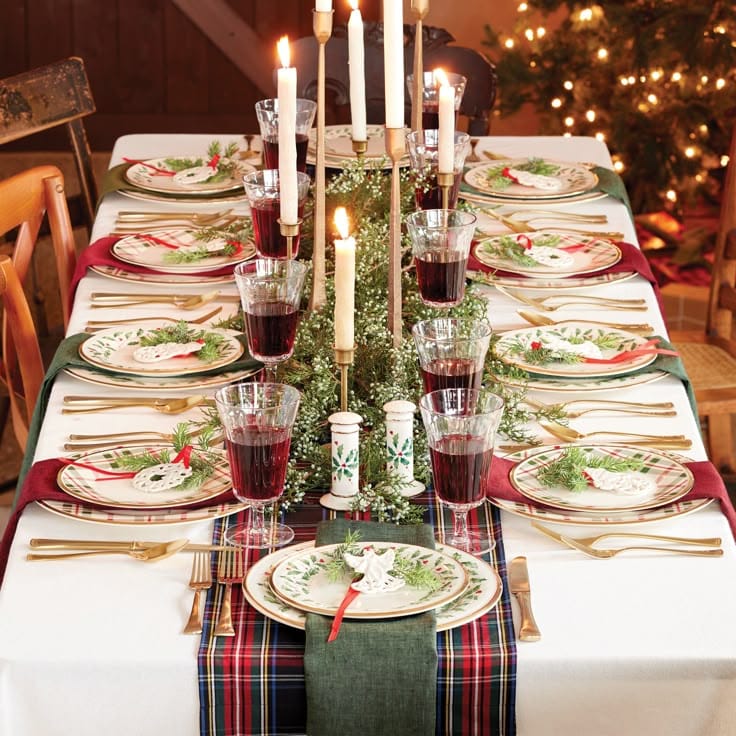 Festive holiday table setting with candles, elegant plates, and wine glasses, decorated with greenery and Christmas accents.