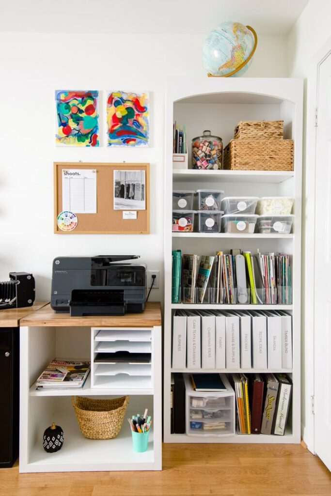 Organized home office space with printer, shelves, colorful decor, and globe on white background.