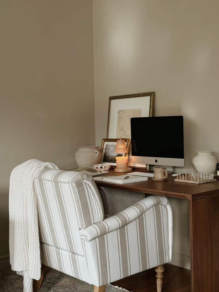 Cozy home office with striped chair, wooden desk, computer, and warm lighting, perfect for a productive work environment.