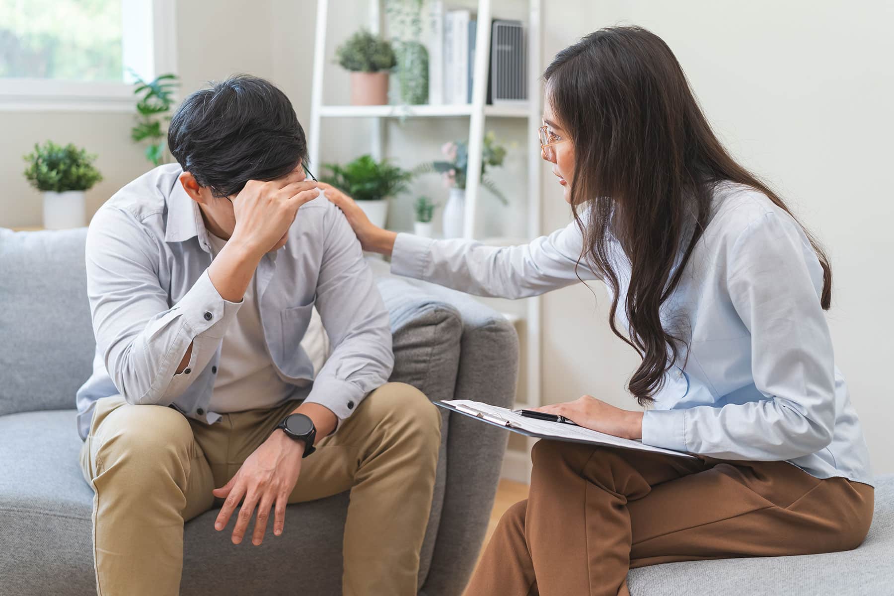 Therapist comforting a man during a counseling session on a sofa, offering emotional support and understanding.