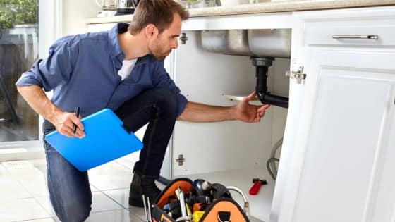 How Local Plumbers in Whittier Extend the Life of Garbage Disposal Systems Man inspecting kitchen sink plumbing with a toolbox nearby, holding a blue folder. | Sky Rye Design Man inspecting kitchen sink plumbing with a toolbox nearby, holding a blue folder.
