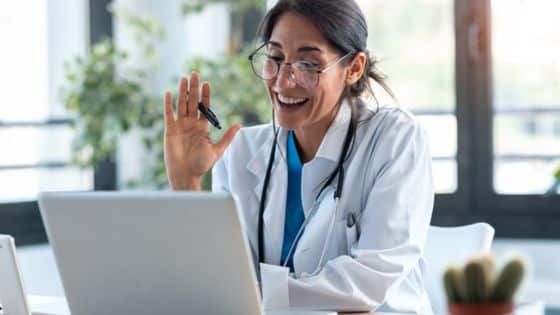 How Medical Practices Are Building Better Patient Experiences Without Adding Square Footage Smiling doctor in a white coat waves during a video call on a laptop in a bright clinic. | Sky Rye Design Smiling doctor in a white coat waves during a video call on a laptop in a bright clinic.