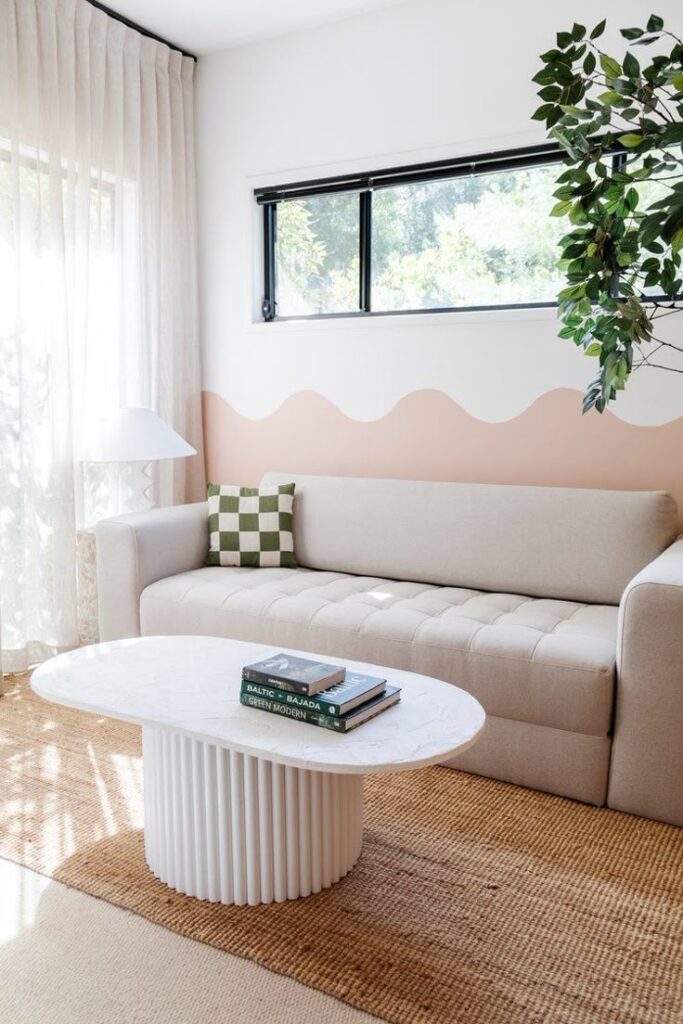 Modern living room with beige sofa, patterned pillow, white coffee table, and large plant for a cozy vibe.