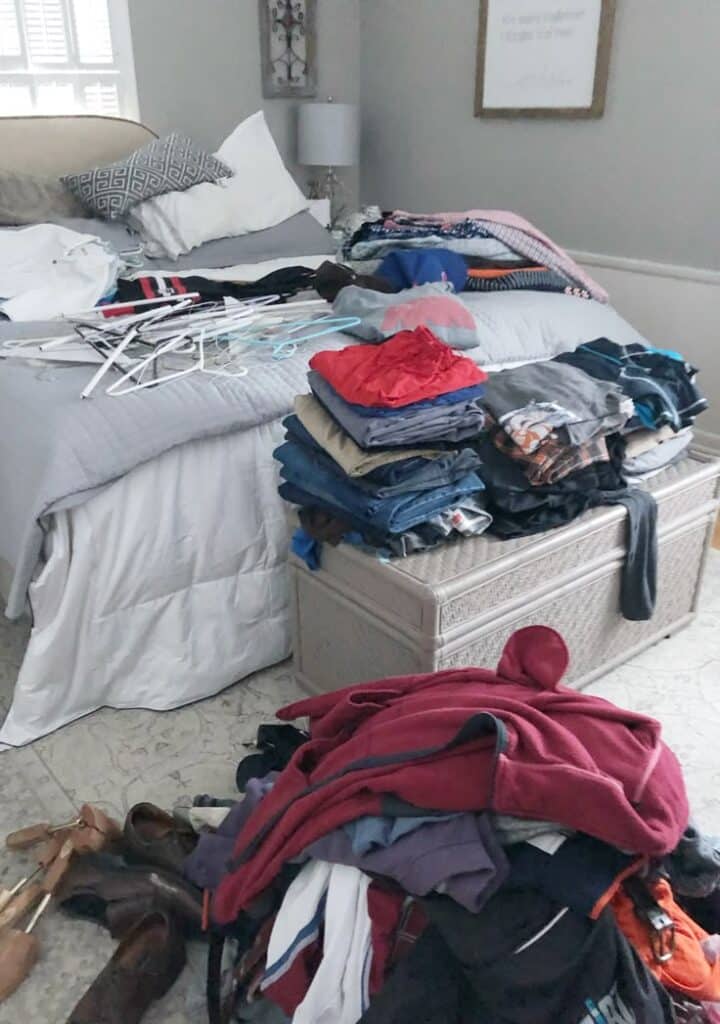 Messy bedroom with clothes stacked on bed and chest, hangers scattered, needing tidying and organization.