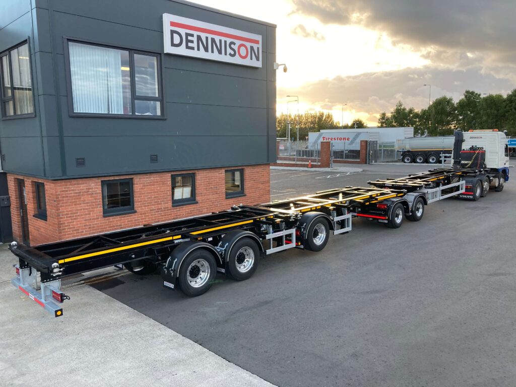 Long truck trailer parked beside Dennison building at sunset.