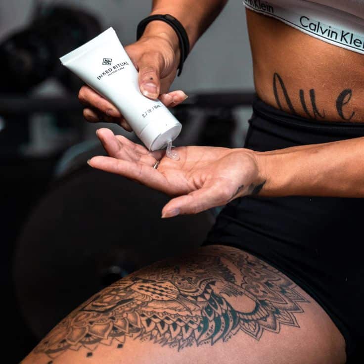 Person applying Inked Ritual tattoo aftercare lotion on hand, highlighting detailed leg tattoo design.
