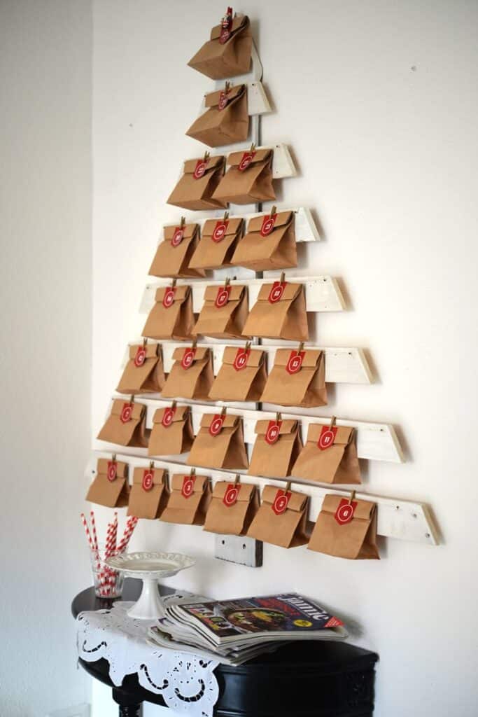 Il calendario dellAvvento DIY Christmas advent calendar shaped like a tree with numbered bags on a wall, next to a table with straws and magazines. | Sky Rye Design DIY Christmas advent calendar shaped like a tree with numbered bags on a wall, next to a table with straws and magazines.