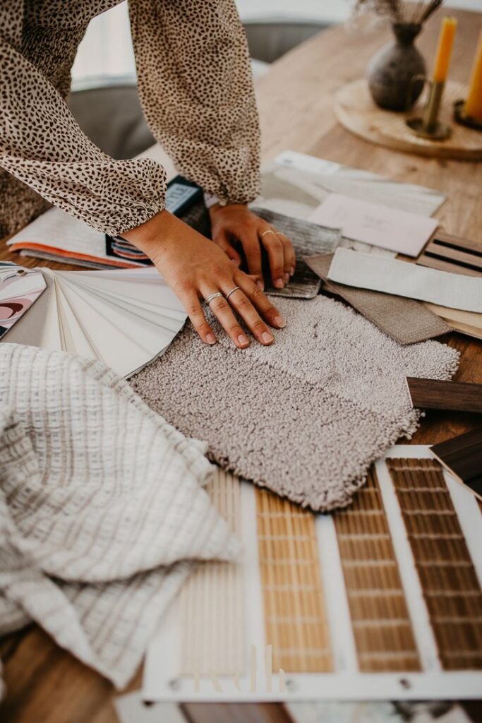 Interieur ontwerp woonkamer _ interieur ideeën woonkamer Person selecting fabric and flooring samples on a table for interior design inspiration. | Sky Rye Design Person selecting fabric and flooring samples on a table for interior design inspiration.