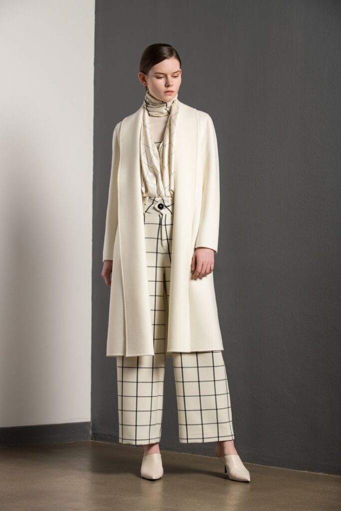 Woman in stylish white outfit with grid-patterned pants, standing against a gray wall. outfit