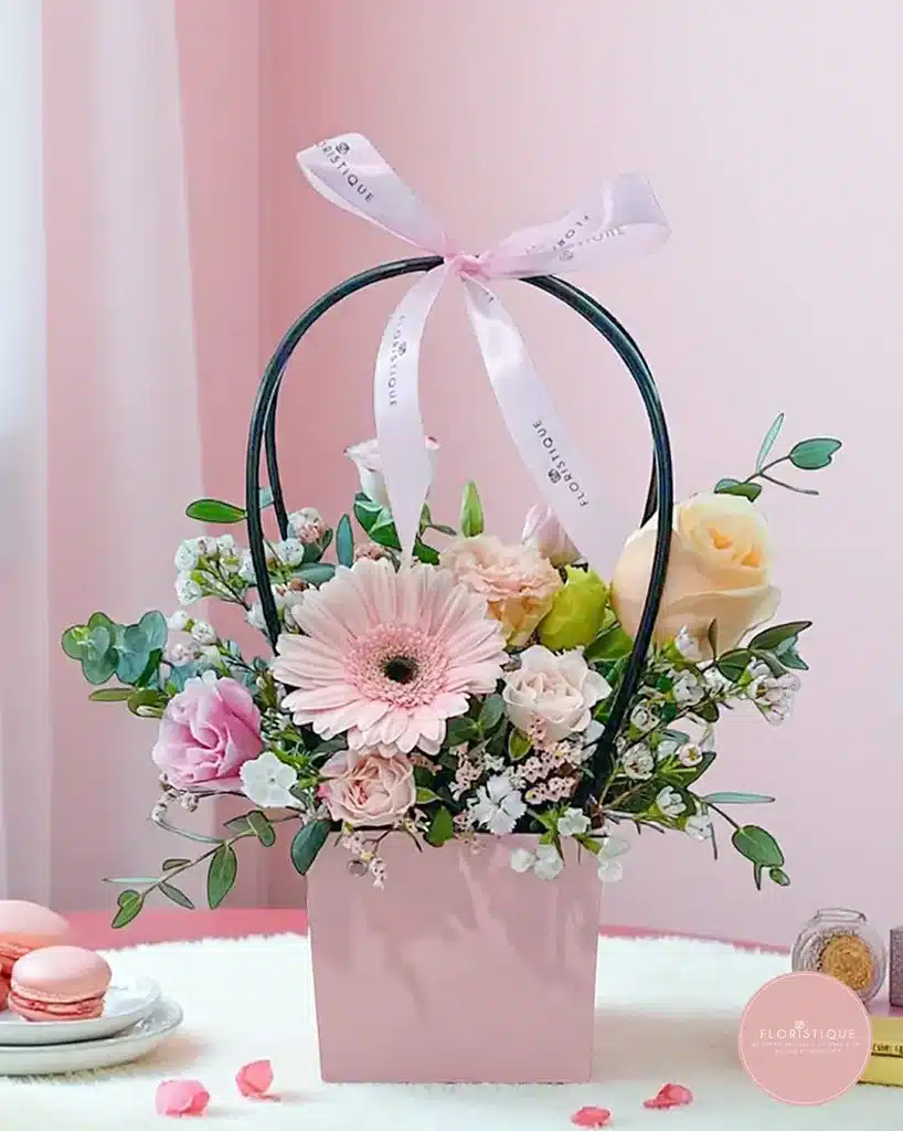 Pink floral arrangement with roses and daisies in gift bag, accented by a bow. Bright, elegant, perfect for special occasions.