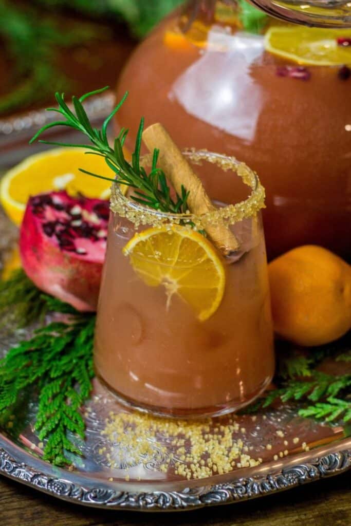 Festive holiday punch with orange slice, cinnamon stick, and rosemary garnish on a decorative serving tray.