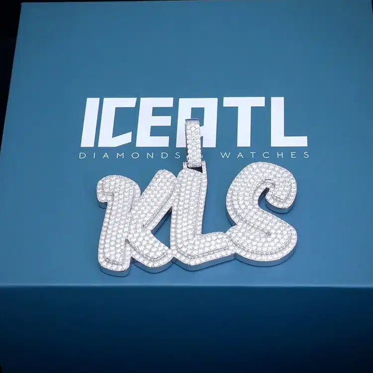 Diamond-encrusted KLS pendant on a blue ICE ATL box, showcasing luxury jewelry and branding.