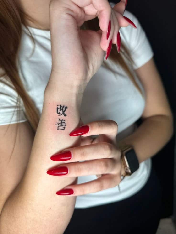 Kaizen tattoo Close-up of a tattooed wrist with red nails and Kanji characters, wearing a white shirt and smartwatch. | Sky Rye Design Close-up of a tattooed wrist with red nails and Kanji characters, wearing a white shirt and smartwatch.
