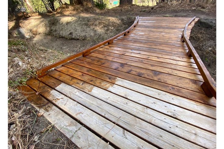 Keeping cedar stunning_ Pro tips for caring for your deck _ Produced by Seattle Times Marketing Wooden footbridge on a nature trail with sunlight highlighting fresh stain, surrounded by trees and dry underbrush. | Sky Rye Design Wooden footbridge on a nature trail with sunlight highlighting fresh stain, surrounded by trees and dry underbrush.
