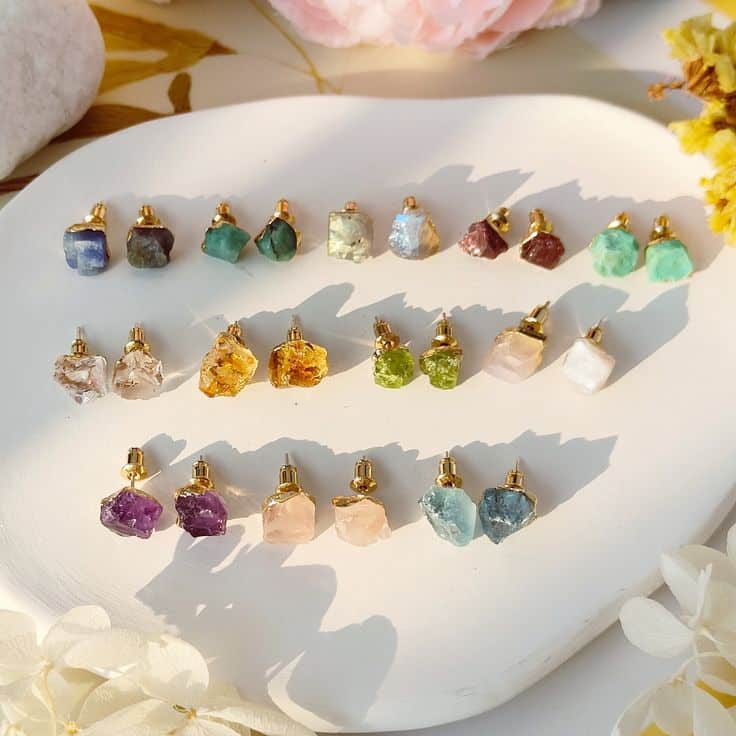 Colorful gemstone stud earrings displayed on a white plate, illuminated by natural sunlight.