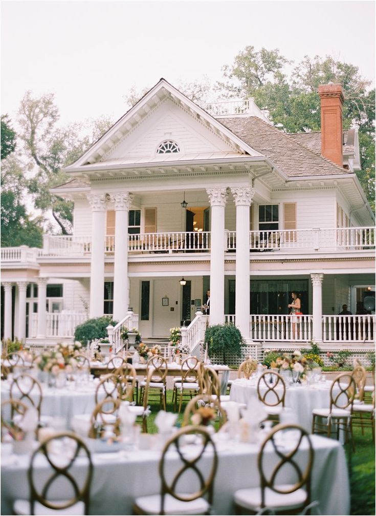 Elegant outdoor wedding reception at a historic white mansion, decorated tables and chairs on a lush green lawn.