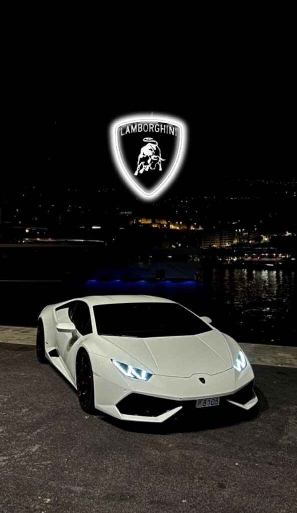 White Lamborghini parked by the waterfront at night, with illuminated logo above.