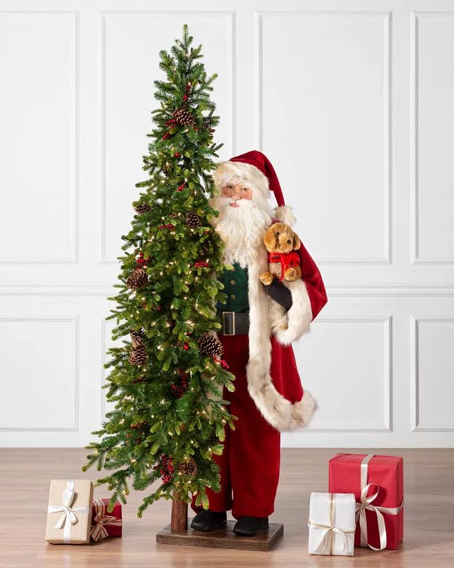 Santa Claus with a teddy bear beside a decorated Christmas tree and gift boxes in a festive setting.