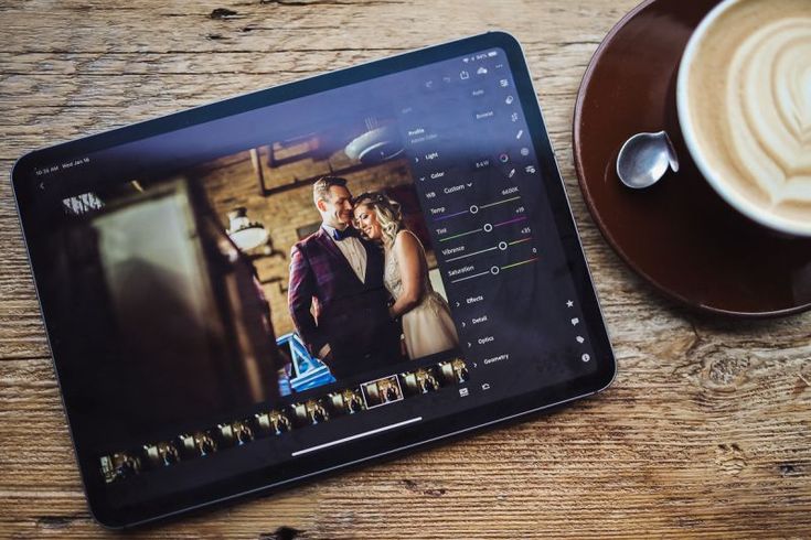 Tablet editing wedding photo beside a latte on wooden table.