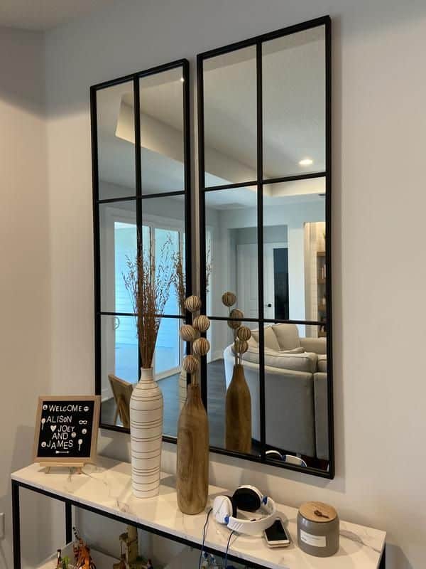 Decorative hallway mirrors with plants and a welcome sign on a table, reflecting a cozy living room.